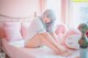 A woman sitting on a bed with a pink stuffed animal.