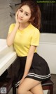 A woman in a yellow shirt and black skirt posing for a picture.