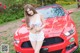 A woman posing in front of a red sports car.