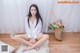 A woman sitting on a white rug next to a vase of flowers.