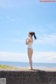 A woman in a white bikini standing on a concrete wall by the ocean.