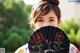 A woman holding a black fan with red flowers on it.